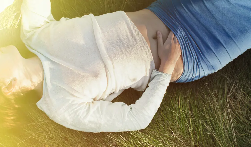 Ein Bild von einer Person, die in den Feldern liegt, wobei ihre Hand in Richtung ihrer erogenen Zone gleitet.